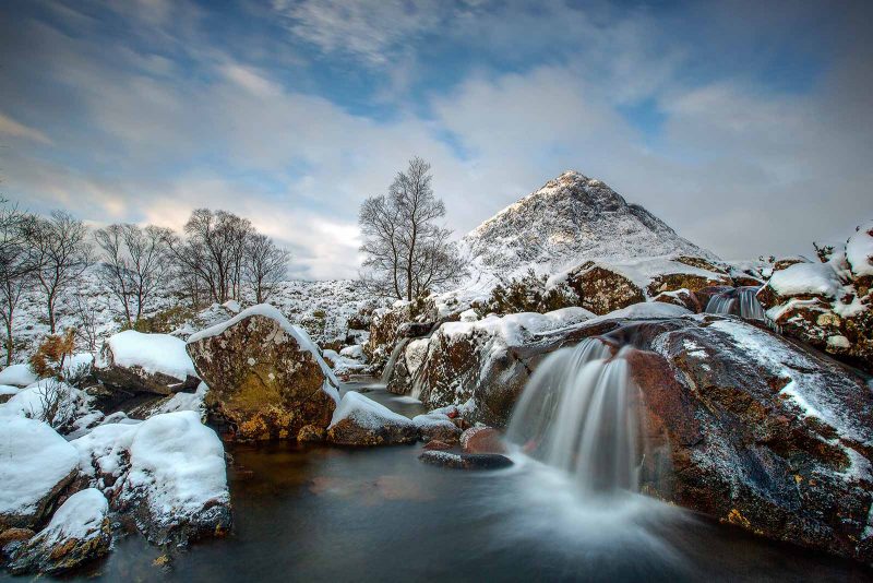 a partially frozen waterfall with plenty of background interest including mountain