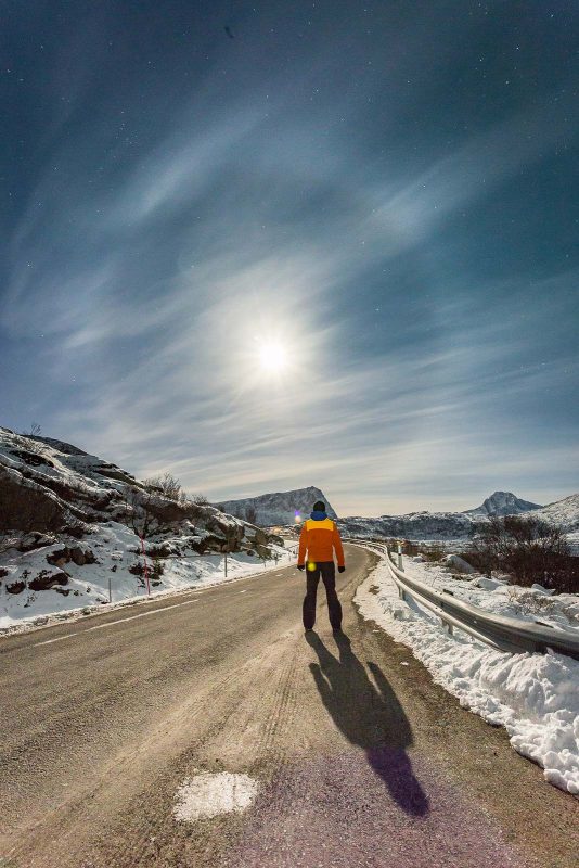 moonbow behind a road with person standing in the middle