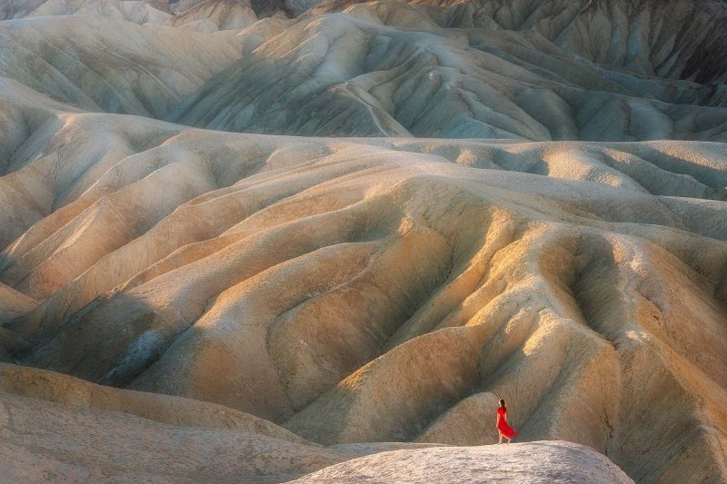 A woman in a red dress stands in front of a desert mountain landscape